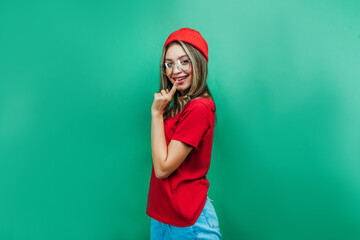 Stylish young girl in the studio on a green background looks into the camera with a concerned look and in transparent glasses. Background