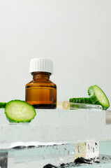 Closeup of glass brown bottle of beauty product, slices of fresh juicy cucumber on the wet glass platform against white background