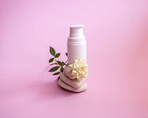 white plastic jar with  dispenser and  gentle caring organic hand and body cream, on smooth textured rounded stones on  pink background with  small room living white rose.