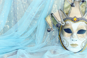 Photo of elegant and delicate Venetian mask over pastel blue and gold chiffon background