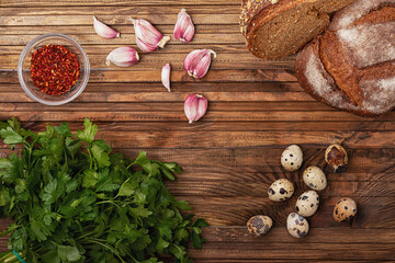 quail eggs,  rosemary, garlic, cereal bread and a plate of paprika on a wooden table
