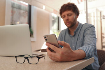 Handsome man using smartphone at table in cafe, focus on hand