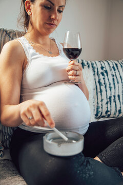 A pregnant woman drinking wine and smoking cigar at home. Unhealthy lifestyle.