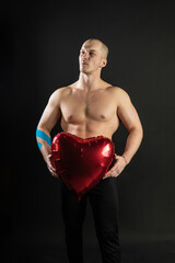 Athletic man holding a red heart, a naked balloon in his hand for a day of velentin pumped up, bodybuilder romantic. lover guy LGBT. In the studio on a black background Joyful with tender lips