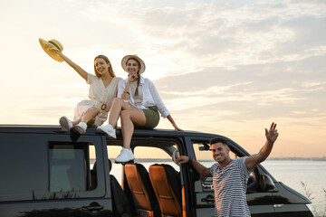 Happy friends near sea at sunset. Summer trip