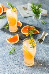Two glasses of Paloma cocktails with tequila fresh grapefruit juice combined and rosemary. Gray concrete surface.