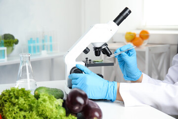 Scientist inspecting slice of cucumber with microscope in laboratory, closeup. Poison detection