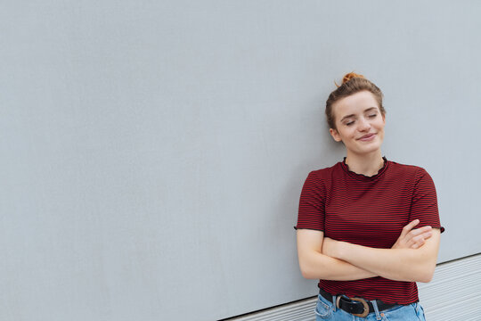 dreaming youg woman with folded arms leans against a wall