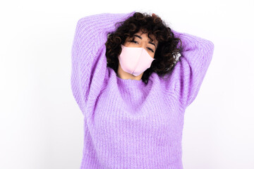 young beautiful caucasian woman wearing medical mask standing against white wall stretching arms, relaxed position.