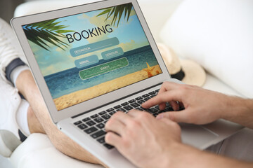 Man booking tickets online on sofa indoors, closeup. Travel agency concept