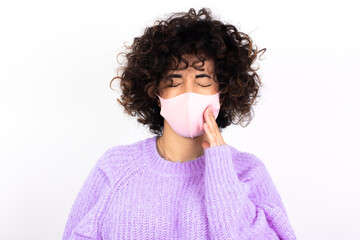 young beautiful caucasian woman wearing medical mask standing against white wall touching mouth with hand with painful expression because of toothache or dental illness on teeth.
