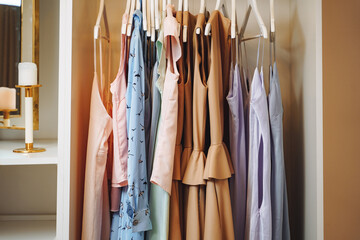 Women's clothing dresses and blouses on hangers in a dressing room or store.