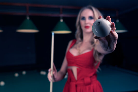 in the foreground there is a billiard ball with the number seven and a sexy blonde holding its image which is out of focus