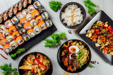 High angle shot of plates with traditional Asian food, seafood, and sushi on a table..
