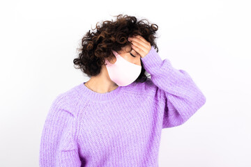 A very upset and lonely young beautiful caucasian woman wearing medical mask standing against white wall crying,