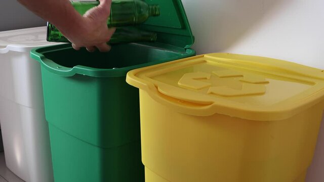 The man throws trash into the one of three dustbins
