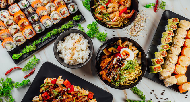 High Angle Shot Of Plates With Traditional Asian Food, Seafood, And Sushi On A Table..