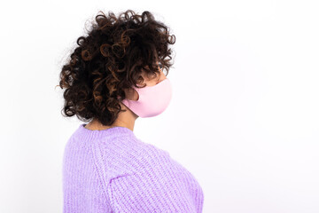 The back side view of a young beautiful caucasian woman wearing medical mask standing against white wall. Studio Shoot.