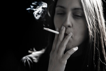 Young woman smoking cigarette on black background