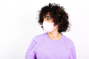 young beautiful caucasian woman wearing medical mask standing against white wall stares aside with wondered expression has speechless expression. Embarrassed model looks in surprise