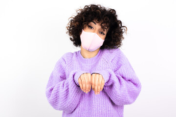 young beautiful caucasian woman wearing medical mask standing against white wall makes bunny paws and looks with innocent expression plays with her little kid