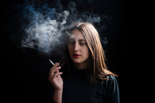 Young woman smoking cigarette on black background