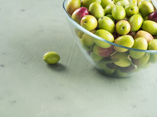 Freshly picked raw green olives in glass bowl on textured background.