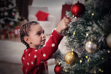 Adorable little child decorating Christmas tree at home