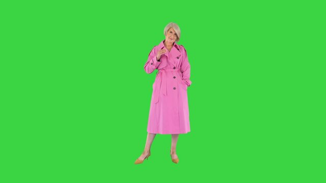 Beautiful stylish senior lady in trench coat posing to camera on a Green Screen, Chroma Key.