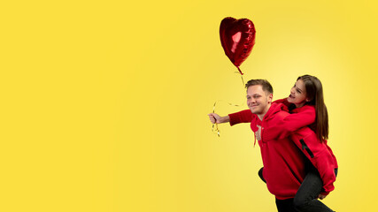 Piggyback, flyer. Beautiful couple in love on yellow studio background. Saint Valentine's Day, love, relationship and human emotions concept. Copyspace. Young man and woman look happy together.