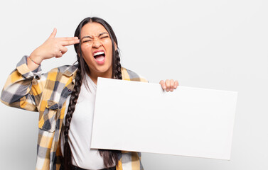hispanic woman looking unhappy and stressed, suicide gesture making gun sign with hand, pointing to...