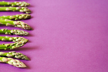 the stems of green raw asparagus are arranged in a row exactly on a purple background side view . vegetable diet