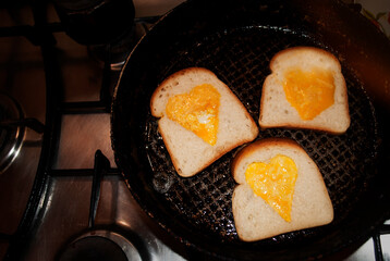 Egg, heart-shaped omelette in toasted slice of gluten-free bread fried in a pan. Valentine's day concept. Homemade creative food. Festive lunch or breakfast. The whip cooking process.