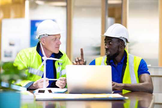 Two engineers African american engineer and caucasian electrician wearing white hard hat working on laptop computer at workplace office. clean and green alternative energy concept.