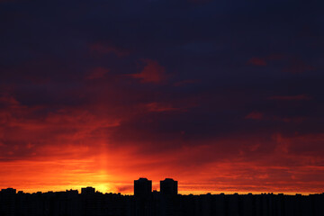 Sunset over city, scenic view. Setting sun and orange sky with dark dramatic clouds above silhouettes of residential buildings