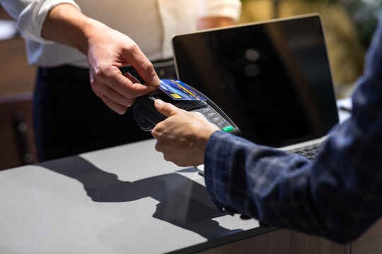 Female receptionist employee holding card reader machine on hand at checkout counter.