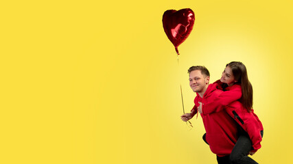 Piggyback, flyer. Beautiful couple in love on yellow studio background. Saint Valentine's Day, love, relationship and human emotions concept. Copyspace. Young man and woman look happy together.
