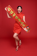Happy Chinese new year. Asian woman wearing traditional cheongsam qipao dress holding Chinese New Year couplets isolated on red background.