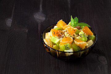 Refreshing fruit salad. healthy salad from fruit with green mint on a wood table. Mixed fresh banana, orange, kiwi, fruit on the black background. copy space.