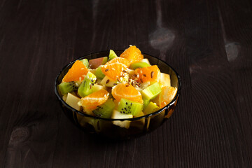 Refreshing fruit salad. healthy salad from fruit with green mint on a wood table. Mixed fresh banana, orange, kiwi, fruit on the black background. copy space.
