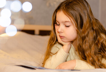 A child, 7-year-old girl with long blonde hair reading a children's book while lying on the couch....