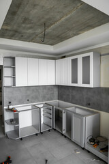 Custom kitchen cabinets installation with a white furniture facades mdf. Gray modular kitchen from chipboard material on a various stages of installation. A frame furniture fronts mdf profile.