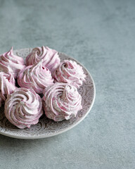 A hand holds a pink marshmallow with marshmallows in the background. Delicious sweets, dessert, healthy homemade sweets. 