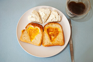 Heart shaped egg omelette in toasted bread slice on white ceramic plate. Valentine's day concept. Festive lunch or breakfast. Copy space.Glass cup in the shape of a heart and double glass.