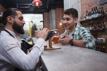 Young cheerful man talking to the bartender at beer pub