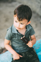 Boy eats ice cream on a stick covered with chocolate, outdoors