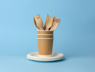 paper cup, white plates and wooden forks and knives on a blue background