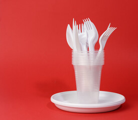 disposable white plastic tableware plates, cups, forks and knives on a red background