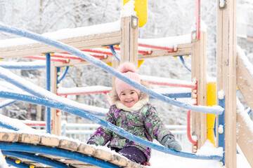 A little girl in winter plays fun in the playground. The girl smiles and looks directly into the frame.