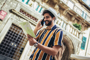 Happy tourist with backpack is making travel across city uses a map for orientation.